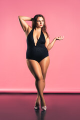 Sexy plus size fashion model in black one-piece swimsuit, fat woman in lingerie on pink background