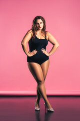 Sexy plus size fashion model in black one-piece swimsuit, fat woman in lingerie on pink background