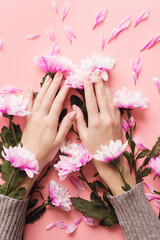 Obraz na płótnie Canvas Delicate young hands on a pink pastel background in a sweater with chrysanthemum flowers in the sleeves. Winter body care concept, moisturizing and wrinkle prevention