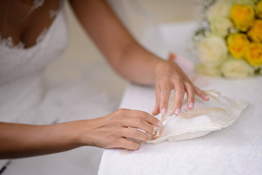 Primo piano delle mani della sposa mentre scioglie il nodo del nastro che trattiene l’anello al cuscinetto porta fedi