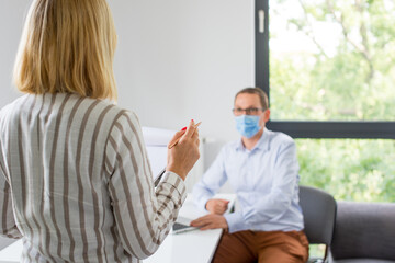 The woman is giving a presentation and the man wearing the face mask. Two business colleagues wearing protective face mask on a meeting during coronavirus. Work in a corporation during a pandemic. 