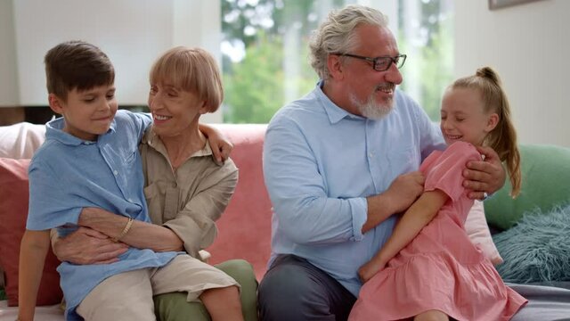 Happy grandfather and grandmother sitting on couch with grandchildren on laps