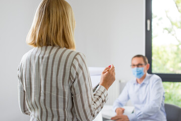 Fototapeta premium The woman is giving a presentation and the man wearing the face mask. Two business colleagues wearing protective face mask on a meeting during coronavirus. Work in a corporation during a pandemic. 