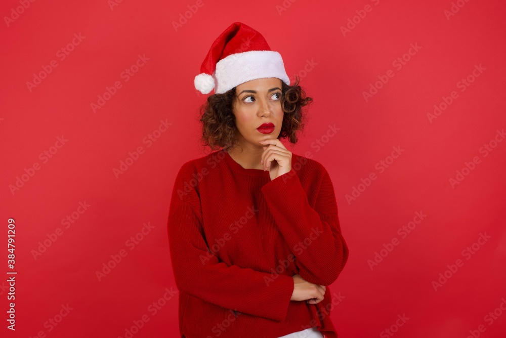 Canvas Prints Shot of contemplative thoughtful Young woman keeps hand under chin, looks thoughtfully upwards, dressed in casual clothes, poses over white background with free space for your text