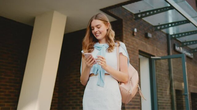Happy young attractive woman walking look around smiling use phone in city center outdoors. Girl with cellphone message communication portrait. Close up. Slow motion
