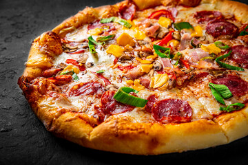 Pizza with Mozzarella cheese, salami, chicken meat, beef, ham, Tomato sauce, pepper, spices. Italian pizza on Dark grey black slate background