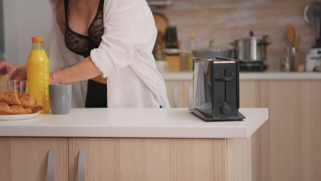 Sexy beatiful woman making roasted bread using toaster wearing black lingerie. Young attractive seductive lady in the morning in cozy interior home preparating delicious and healthy breakfast.