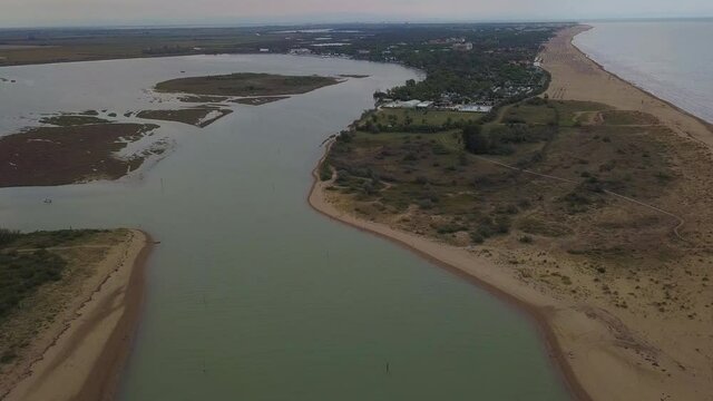 Aerial view of the beautiful lagoon of Caorle towards Bibione in Italy with people enjoying summer at the beach and boats passing by.