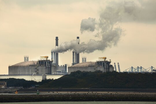 Smoking power plant chimney in an industrial area, oli silos in the foreground