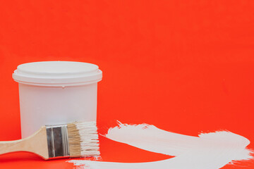 A jar of white paint for repair work and a paintbrush on a red background