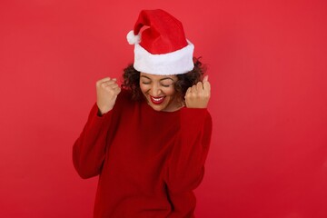 Caucasian brunette woman rejoicing her success and victory clenching her fists with joy. Luckywoman wearing Christmas hat being happy to achieve her aim and goals. Positive emotions, feelings.