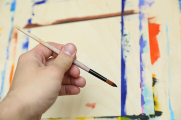 painter's hand holds brush on the background of easel and paints
