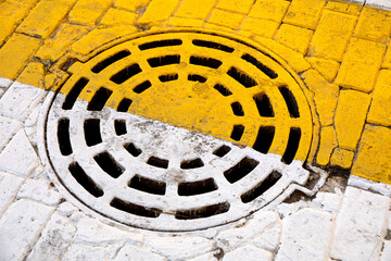 Closed round sewer manhole under yelow and white road marking