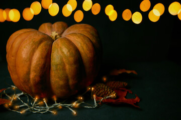 Halloween pumpkin with dry leaves on a black background and with lights in the background