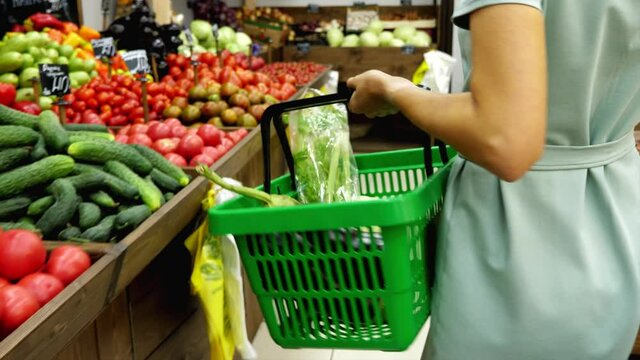 Unrecognizable caucasian woman with shopping basket is walking along rows in grocery store and choosing vegetables, steadicam shot.