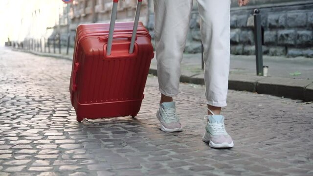 Girl in white jeans walks through the old city with an orange luggage suitcase