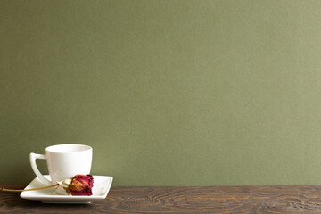 Coffee cup with dry rose flower on wooden table with khaki background