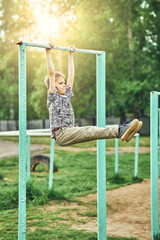 Strong kid doing hanging l-sit on sports ground