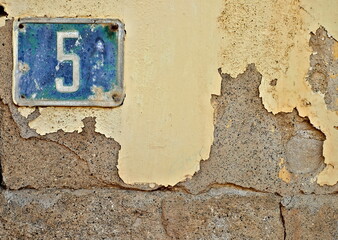 Blue number 5, five, offset in the corner on a weathered aged wall.