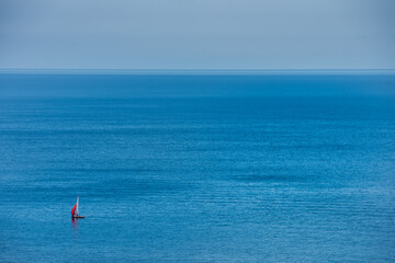 A lonely sailing boat crossing a blue, calm ocean near Mons Klint.The equipage enjoys a relaxing escape away in the Baltic sea. Illustration for sailor, sailing sport and sailing team - Mon, Denmark