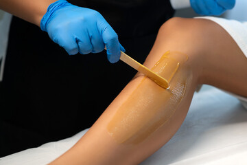 Applying warm wax. Resolute salon worker having depilation procedure and covering legs with special wax material