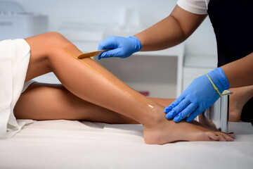 Cosmetologist beautician waxing female legs in the spa center beauty salon cosmetology concept - obrazy, fototapety, plakaty