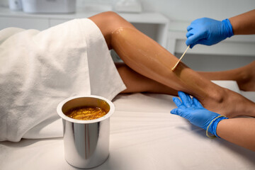 Sugar and waxing depilation of the feet in the beauty salon. Rid of hair on the legs. Sugaring. Master cosmetologist removing hair on the legs. Beautician in the spa center. Cosmetology concept.