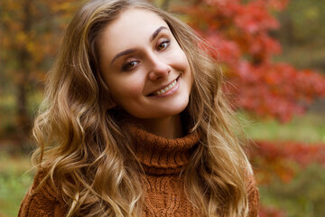 Young happy beautiful woman with curly hair wearing  sweather having good time in autumn park