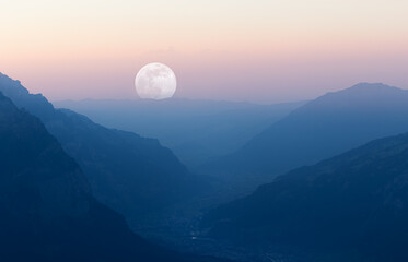 Sunset with layered mountain landscape and moon at end of valley.