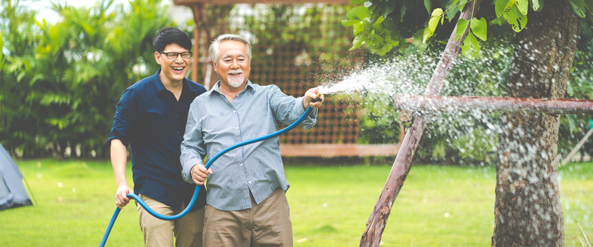Elderly Asian father and Adult son Happy family in backyard watering plant with hose.