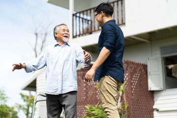 Elderly Asian father and Adult son walking in backyard. Positive Asian man caregiver helping patient