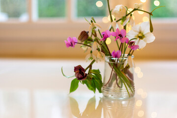 small bouquet of hellebore and snowdrops in glass pot with bokeh