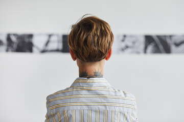 Graphic back view portrait of tattooed young woman looking at paintings at contemporary art...