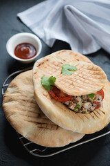 Grilled pitas filled with doner meat and vegetables, vertical shot on a black stone background,...