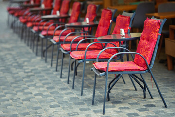Chairs and tables in row, empty red chairs in restaurant on street terrace. Cafe outdoor terrace waiting for new customers. Global pandemic and quarantine time.