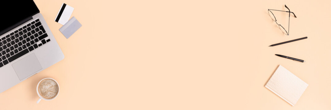 Top view of laptop, mug of coffee, stationery and credit cards on a beige background. Online shopping or e-learning concept. Banner with copy space.