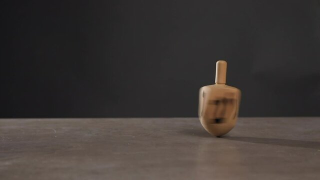 Man spinning dreidel on table against dark background