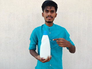 South Indian man in cyan color shirt pointing white color detergent bottle with his fore...