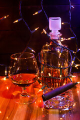 BOTTLE AND GLASS OF BORBON WITH CIGAR AND CHRISTMAS LIGHTS AND COLORED LIGHTS ON WOODEN TABLE AND DARK BACKGROUND