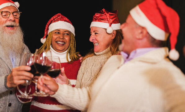 Multiracial senior people wearing christmas hats and cheering with red wine