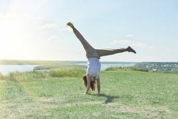  toned fit woman of mid age turning handsprings or cartwheel on a river bank. sunny weather and pleasant landscape. cheerful mood. outdoors workout and gymnastics.