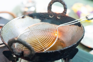 Empty old chipped deep frying pan with oil filled and a wire sieve placed ready to make and fry food