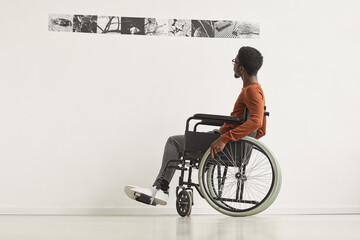 Graphic full length portrait of young African-American man using wheelchair and looking at...