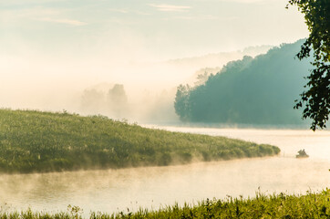 thick morning fog in the summer forest near the reservoir. fishermen on a boat - 384807406