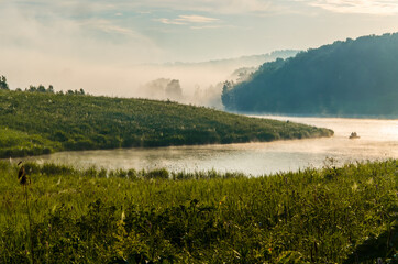 Obraz premium thick morning fog in the summer forest near the reservoir. fishermen on a boat