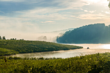 thick morning fog in the summer forest near the reservoir. fishermen on a boat