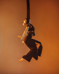 young girl in black costume is making aerial trick on the beige background in photo studio in warm and cold lights, sport concept, free space