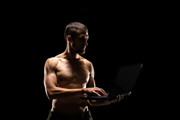 Strong muscular man holding laptop isolated on black background.