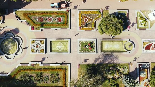 Top view of people walking in a park area with fountains and flower beds per day