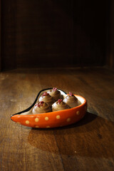 Chocolate pralines toped with rasberry served in a heart shaped bowl on a wooden shelf